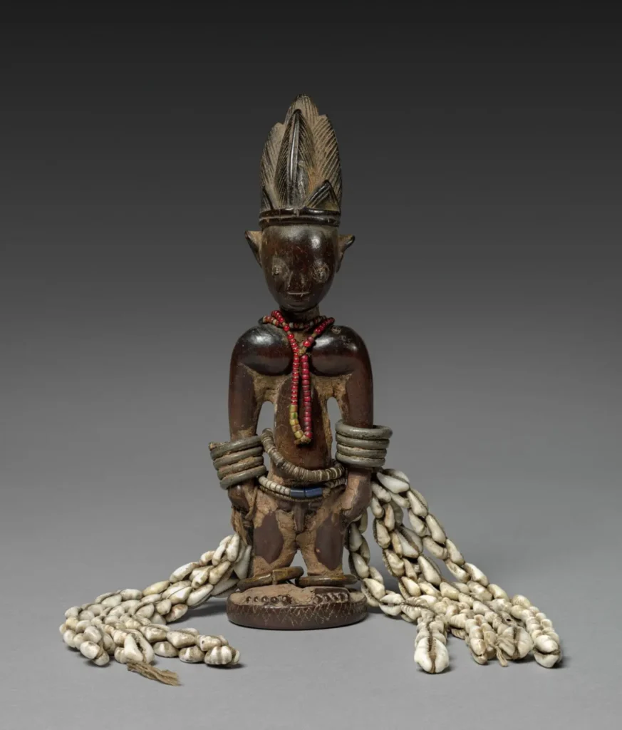 Yoruba Ere Ibeji commemorative sculpture decorated with red beads, metal bracelets, and a long loincloth of cowrie shells. Classical African art from Nigeria, 1875, Cleveland Museum of Art